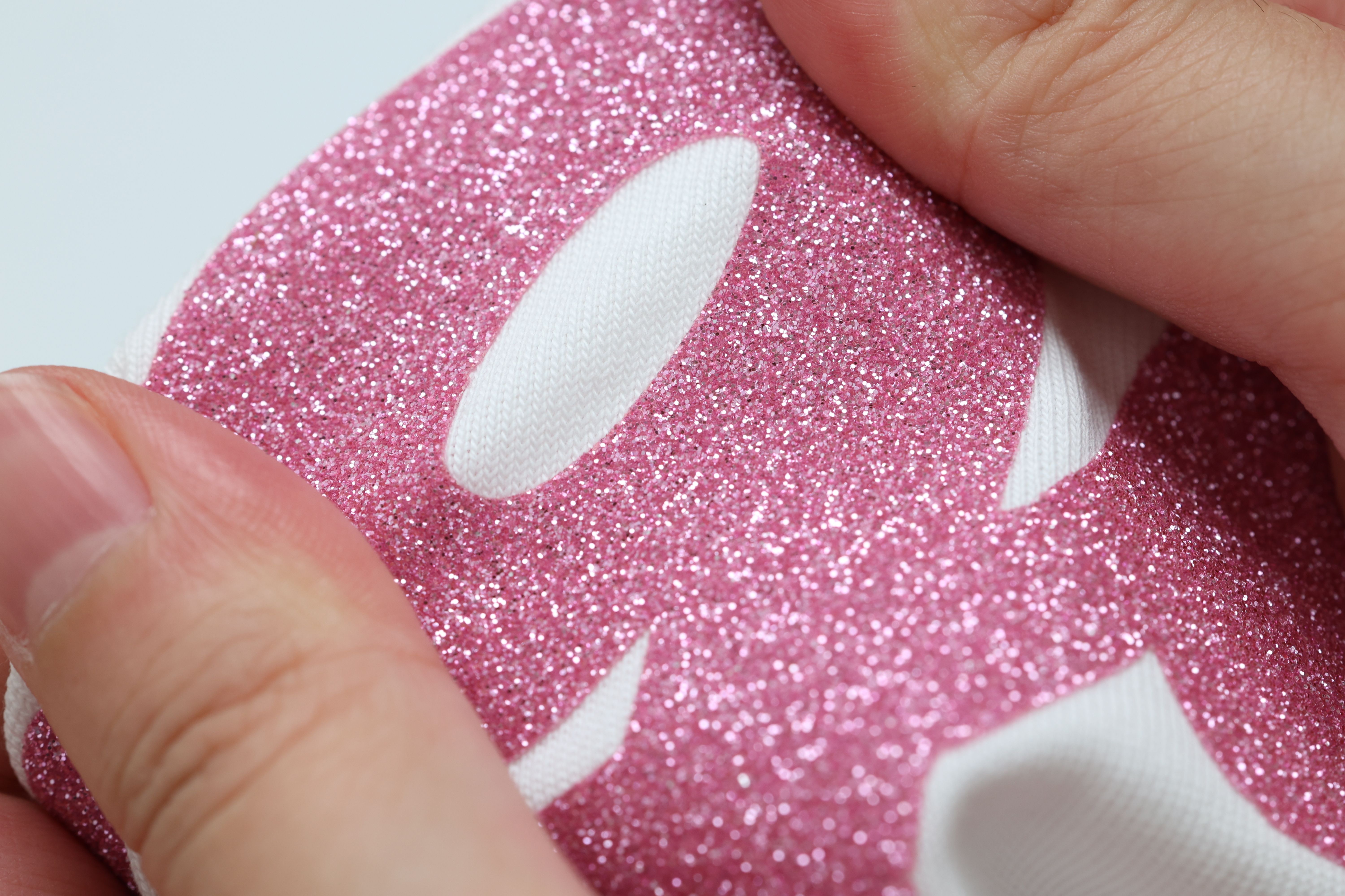 Glitter Heat Transfer Vinyl close-up — pink glitter grain held against knit fabric