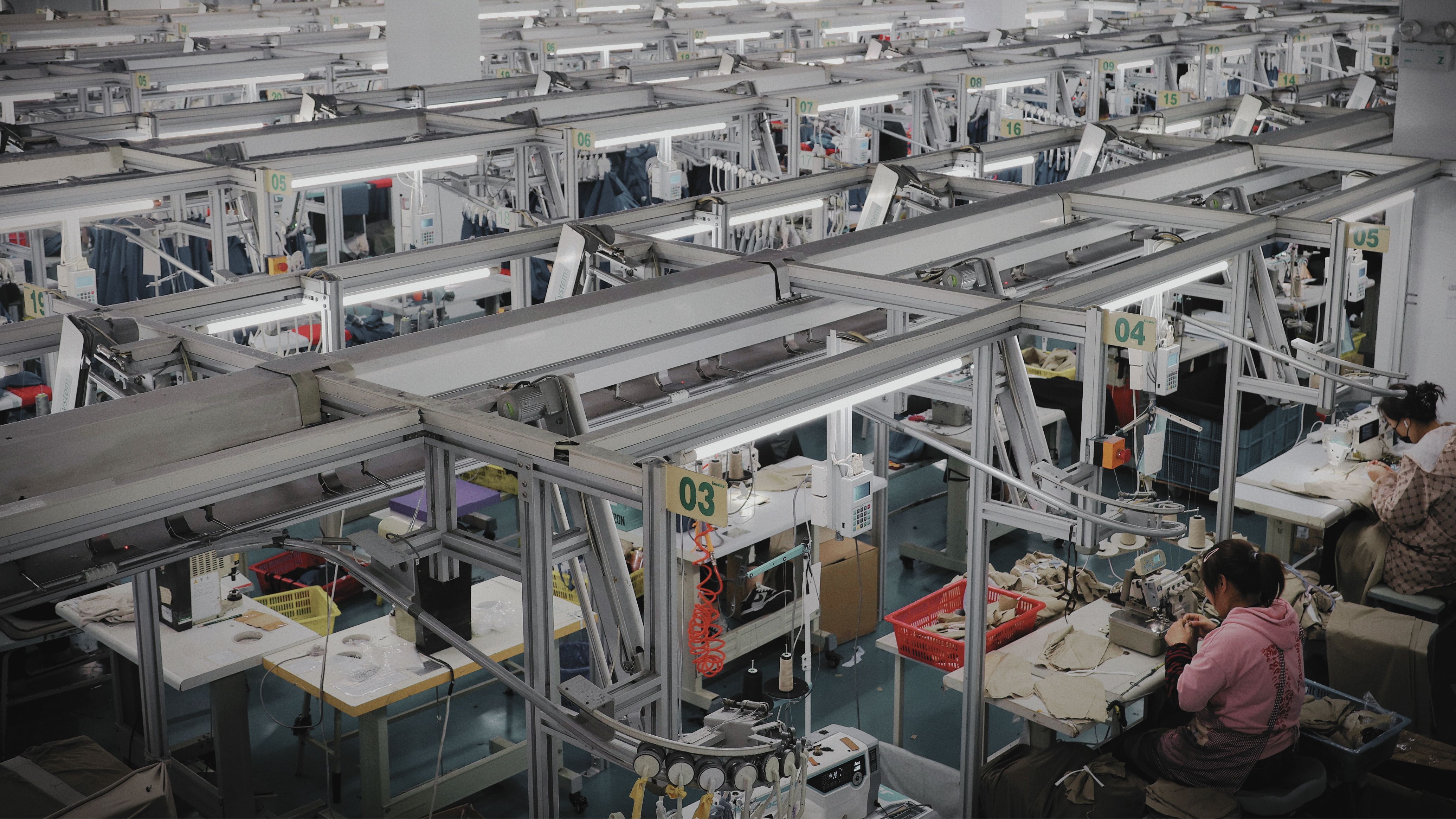 PODpartner vertically integrated POD apparel manufacturing facility - multi-station sewing production line with automated overhead garment transport, demonstrating the in-house factory model that contrasts with aggregator POD platforms Printful and Printi